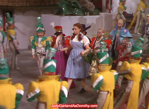 Judy Garland as Dorothy is escorted by the little people and their officials in Munchkinland