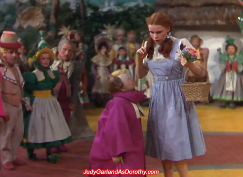 Judy Garland as Dorothy is guided by the Munchkins to the border of Munchkinland